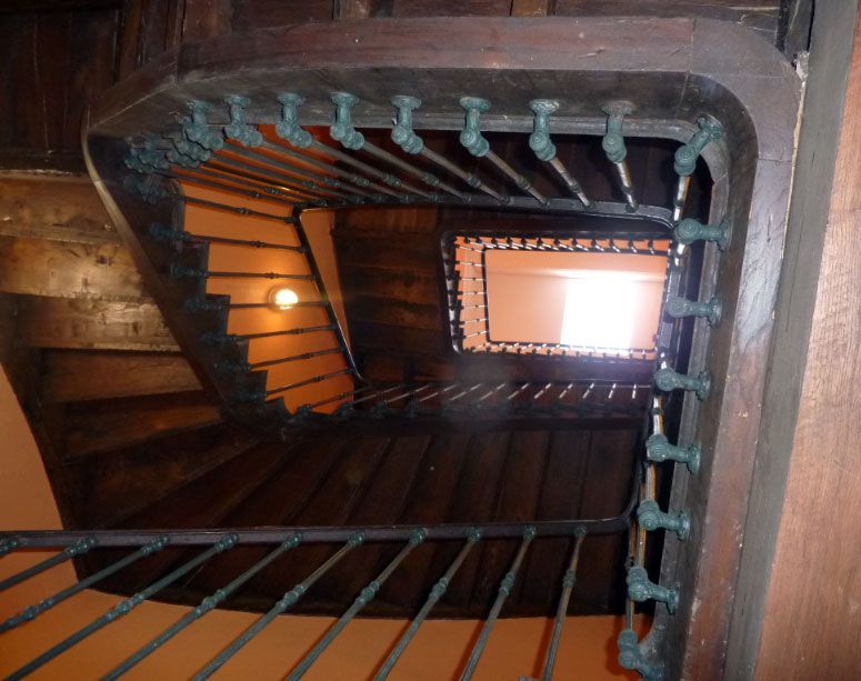 En levant les yeux un escalier en colimaçon en bois sombre avec des rampes en métal.