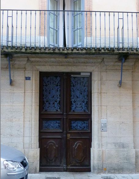 Double porte marron avec ferronnerie décorative bleue, sous un balcon à façade en pierre claire.