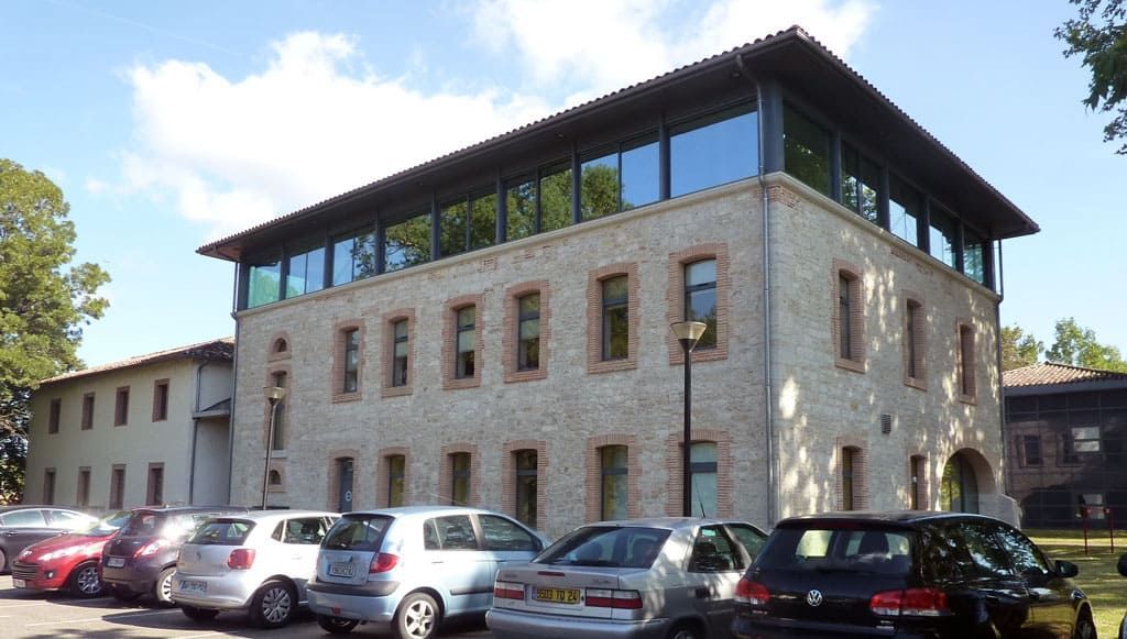 Immeuble en pierre avec un dernier étage vitré, entouré de voitures garées par une journée ensoleillée.