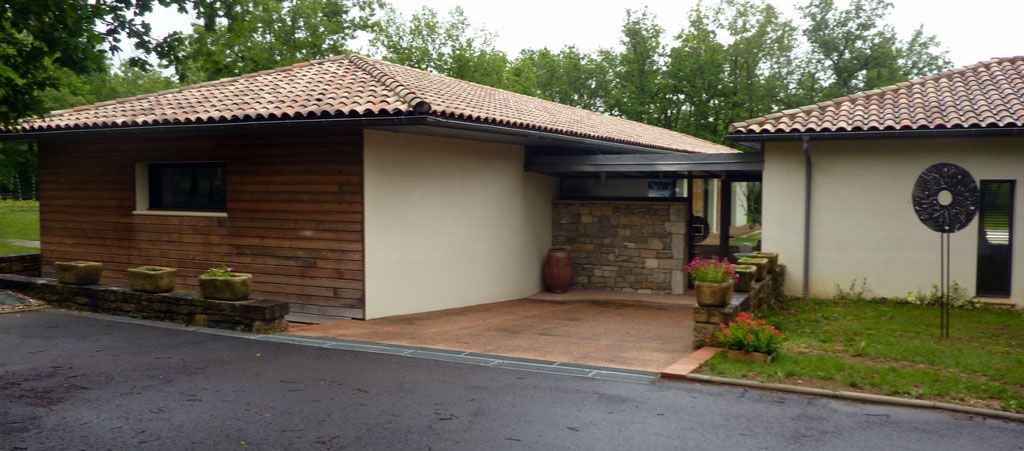 Bâtiments aux toits de tuiles en terre cuite, une partie à façade en bois et une entrée pavée. Une pelouse verdoyante entoure les structures.