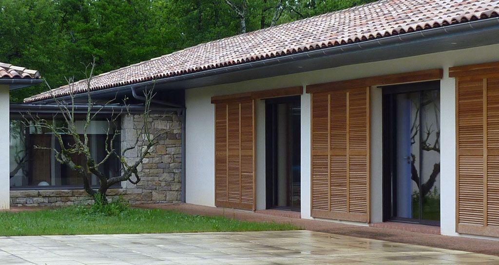 Extérieur d'un bâtiment aux volets bruns et au toit de tuiles, situé sur une pelouse verte.