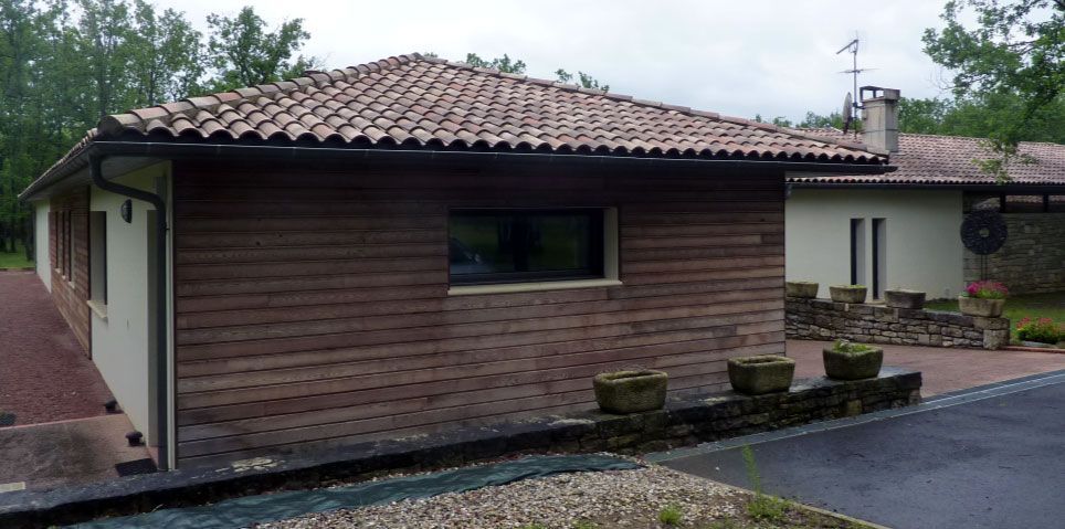 Bâtiments aux toits de tuiles brunes et aux façades en bois. Des arbres verts se dressent à l'arrière-plan.