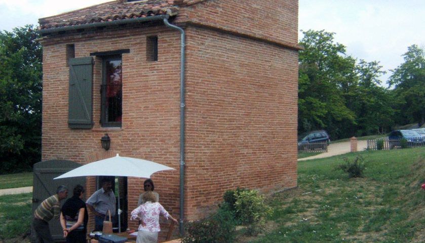 Bâtiment en briques avec une fenêtre ouverte, des volets et un parapluie ; des gens étaient rassemblés à l'extérieur.
