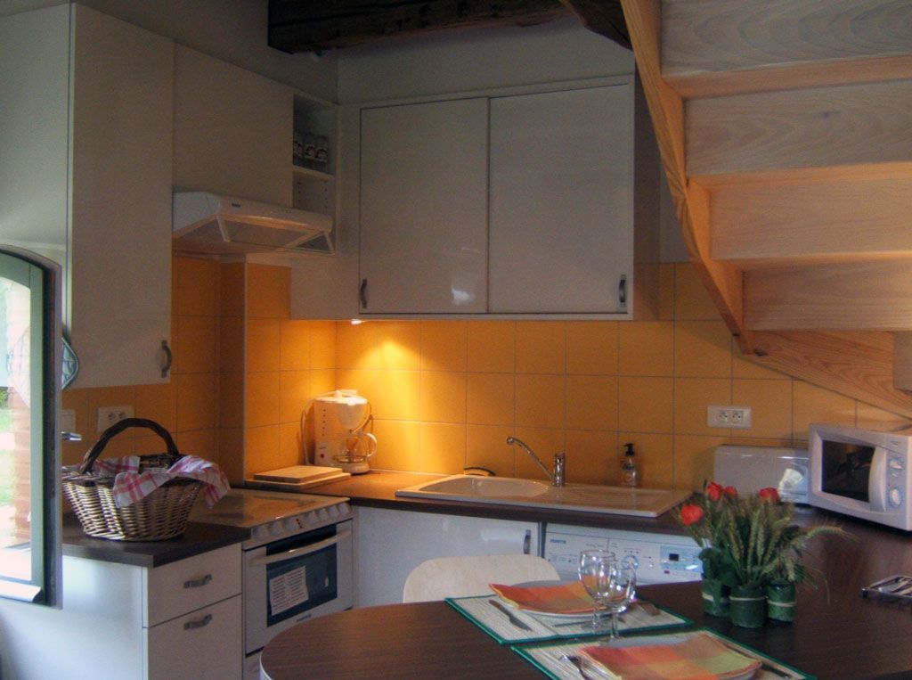 Cuisine avec placards blancs, crédence jaune, électroménager et petit coin repas ; une fenêtre est visible.