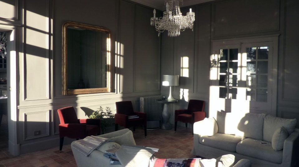 Pièce élégante baignée de lumière naturelle, avec des chaises rouges, un miroir à cadre doré et un lustre en cristal.