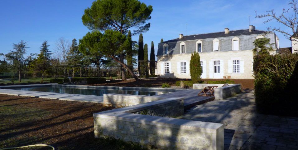 Élégante maison avec piscine dans un cadre ensoleillé. Détails en pierre, arbres et ciel d'un bleu éclatant.