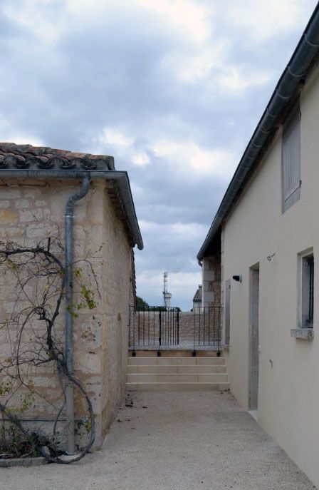 Ruelle étroite entre des bâtiments en pierre et beiges, menant à une structure lointaine sous un ciel nuageux.