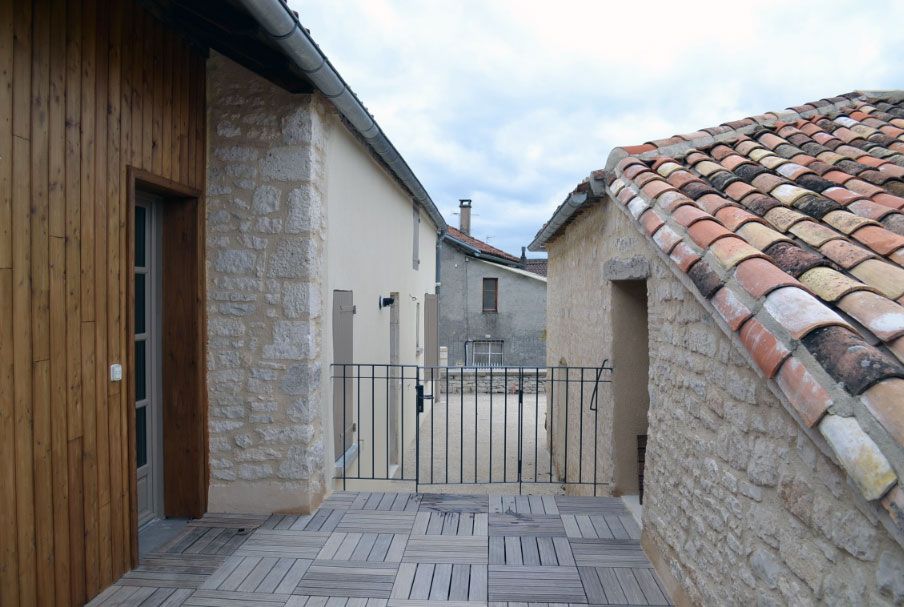 Ruelle étroite en pierre entre des bâtiments, avec un toit de tuiles à droite et un mur en bois à gauche.