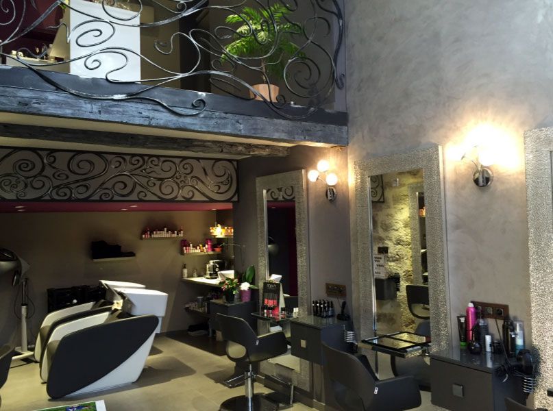 Intérieur d'un salon de coiffure avec postes de coiffage, miroirs et une mezzanine ornée de balustrades décoratives.