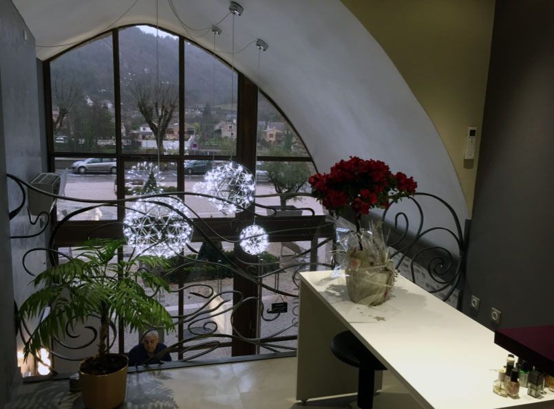 Vue intérieure d'un bâtiment avec une grande fenêtre cintrée donnant sur un paysage urbain. Fleurs rouges sur un comptoir blanc.