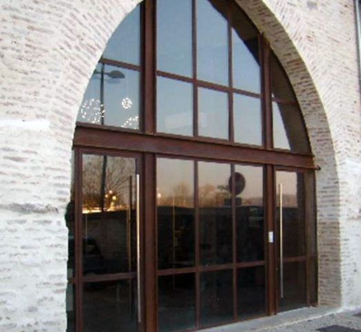 Portes vitrées surmontées d'une fenêtre cintrée, intégrées à un bâtiment en briques. Cadres bruns, verre réfléchissant.