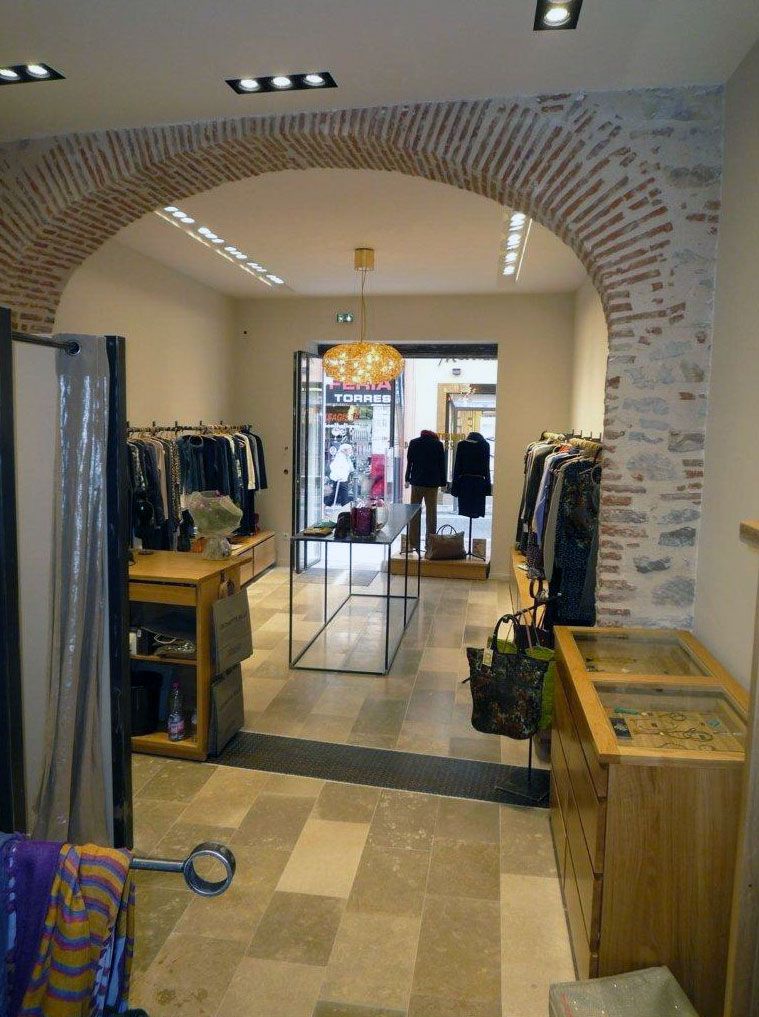 Intérieur d'un magasin de vêtements avec une arche en briques, un sol en pierre et des portants à vêtements.