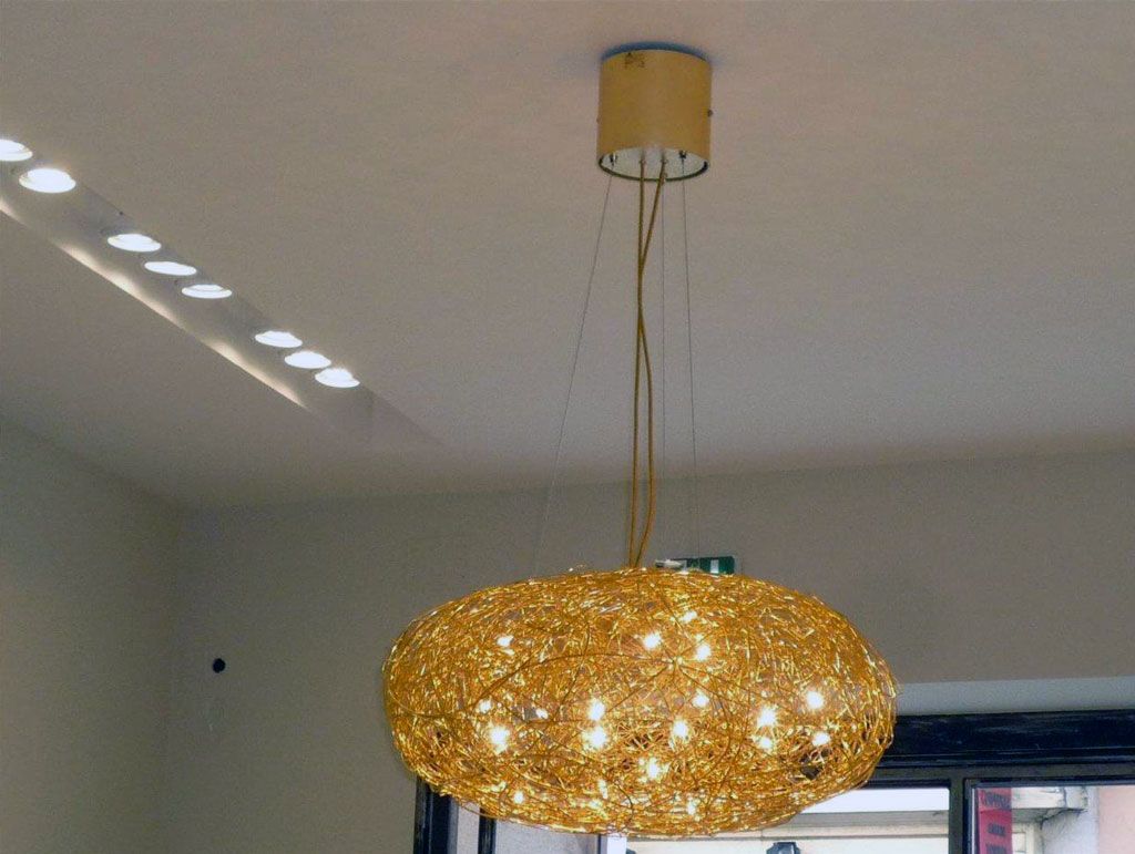 Un lustre sphérique doré, suspendu au plafond, illumine une pièce grâce à des spots encastrés.