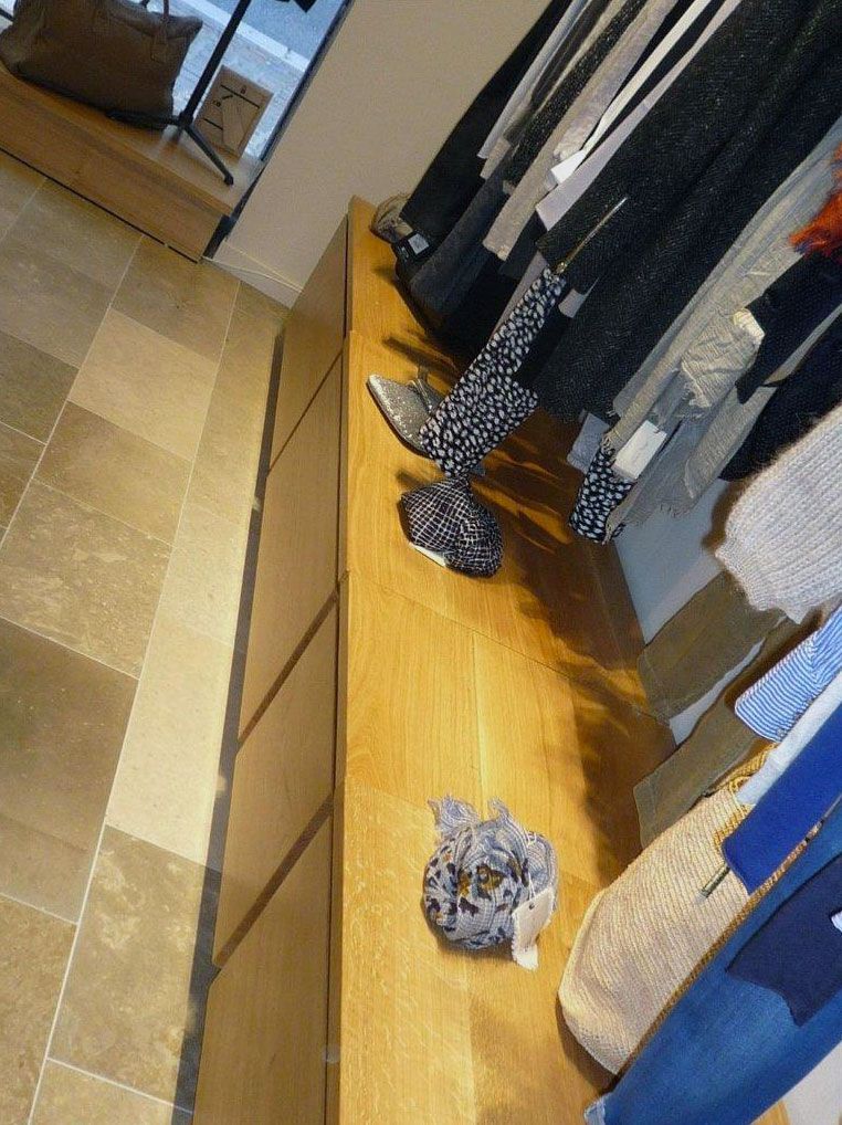 Vêtements exposés dans un magasin, étagères en bois et sol carrelé.