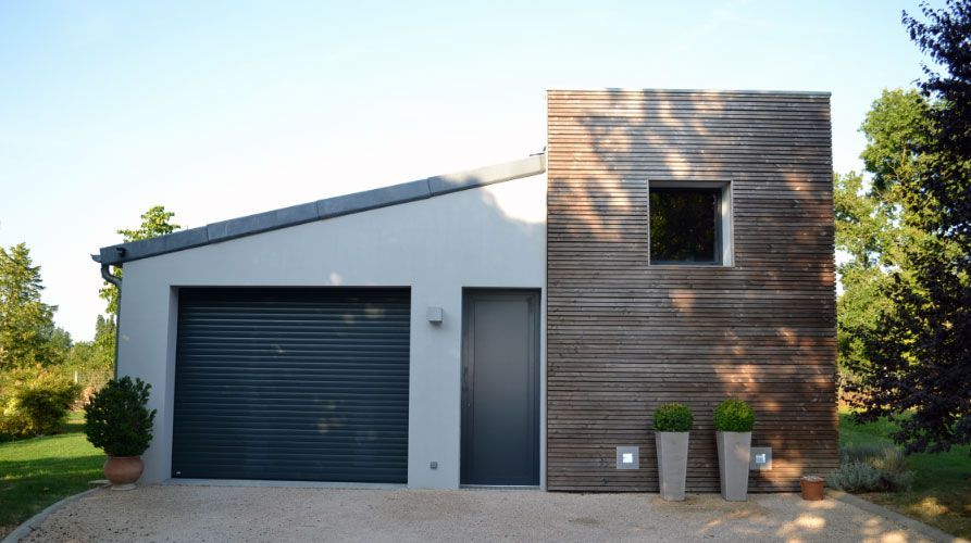 Garage moderne avec façade grise et mur d'accent en bois ; allée de gravier, plantes en pot.