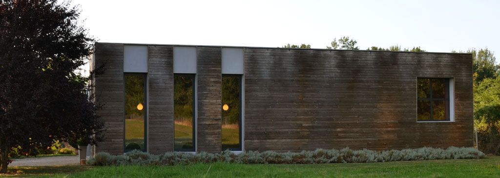 Un bâtiment moderne de forme rectangulaire, avec des fenêtres verticales et une façade texturée horizontale, se détachant sur une pelouse verdoyante.