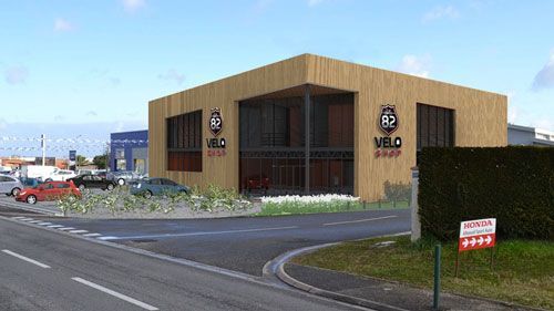 Bâtiment moderne à panneaux de bois avec de grandes fenêtres, logo VELO SHOP. Voitures dans la rue, panneau dans l'herbe.