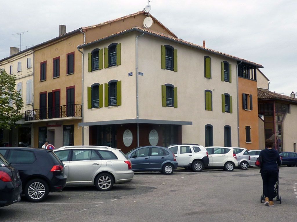 Bâtiments avec des voitures garées devant ; personne marchant avec une poussette.