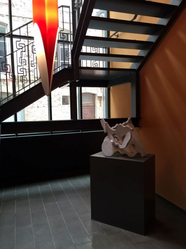 Un escalier aux murs orange, une sculpture sur un piédestal et un luminaire suspendu abstrait rouge et blanc.