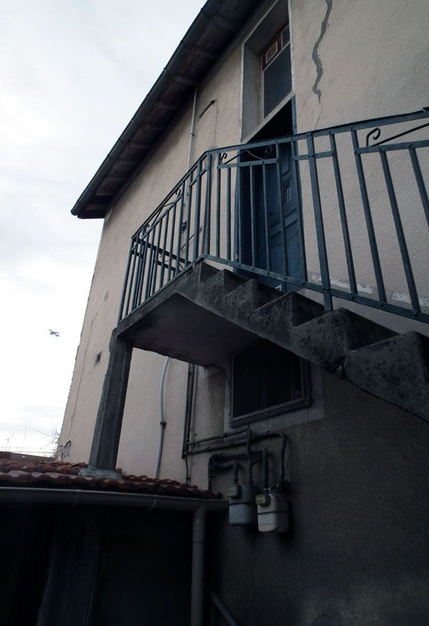 Extérieur d'un bâtiment avec un escalier menant à une porte bleue. Rambarde métallique, murs en stuc et compteurs de gaz visibles.
