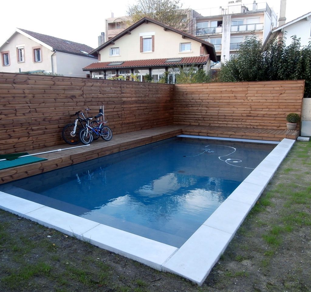 Piscine rectangulaire avec clôture en bois et bordure en pierre ; des vélos sont appuyés contre la clôture sur la terrasse.
