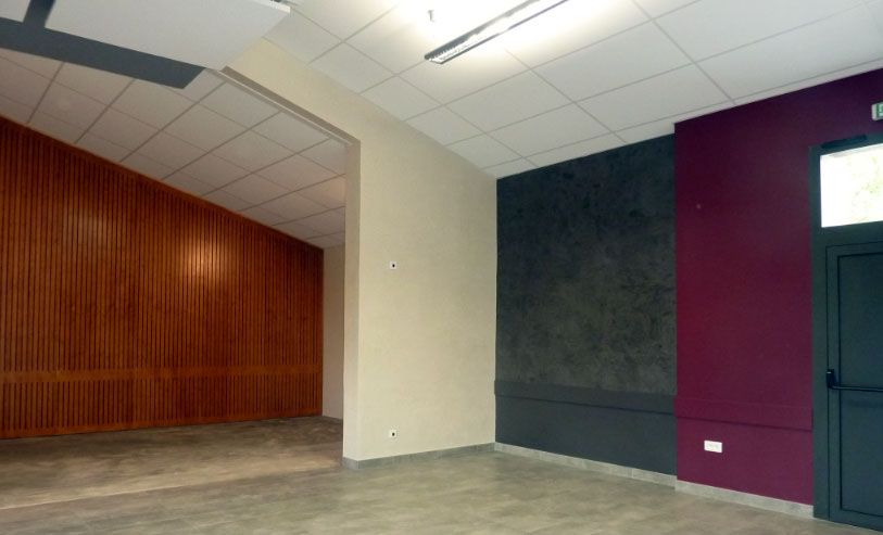 Pièce vide avec lambris, murs beiges, gris foncé et bordeaux, et sol gris.