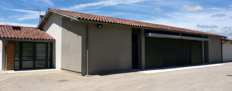 Bâtiment beige avec un toit de tuiles en terre cuite et un ciel bleu.
