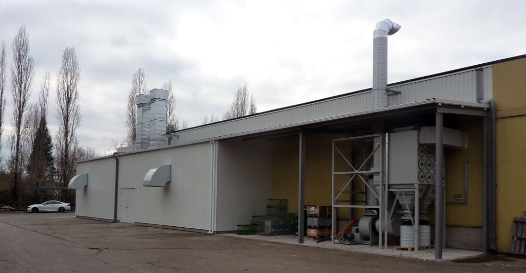 Bâtiment industriel avec des conduits d'aération et un haut tuyau d'échappement se détachant sur un ciel nuageux.
