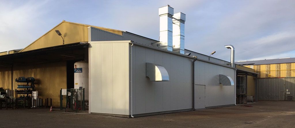 Bâtiment industriel avec cheminées d'évacuation, ventilation et façade grise.