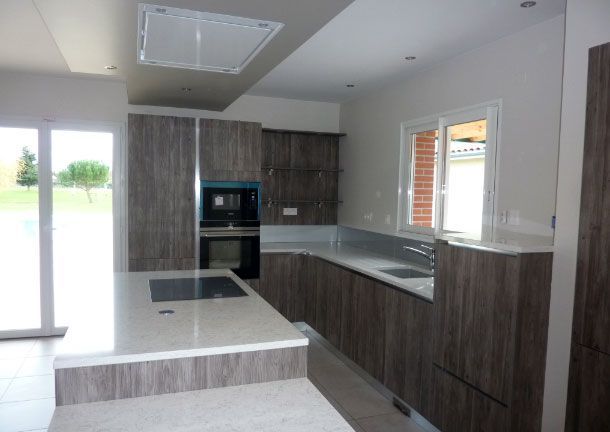 Cuisine moderne avec armoires en bois gris, comptoirs blancs et électroménagers en acier inoxydable.