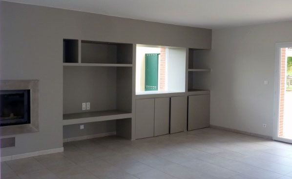Salon peint en gris avec étagères et placards intégrés, cheminée et fenêtre.