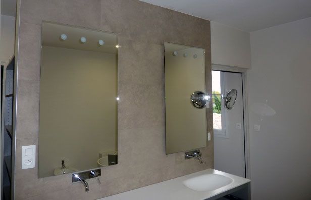 Deux miroirs rectangulaires au-dessus d'un lavabo de salle de bains moderne. Mur beige, plan de travail blanc, robinetterie chromée.