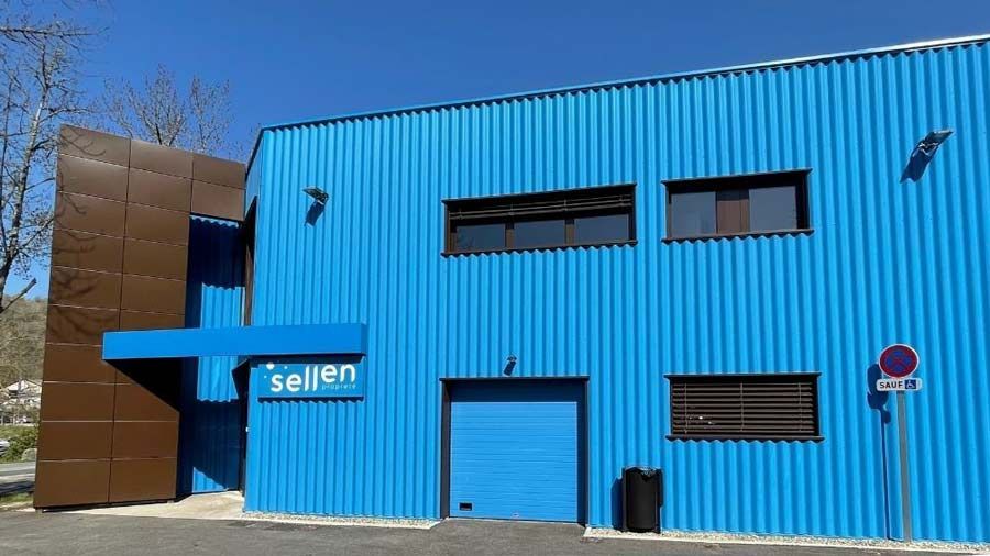 Bâtiment bleu à façade marron ; enseigne « sellan », porte de chargement et fenêtres.