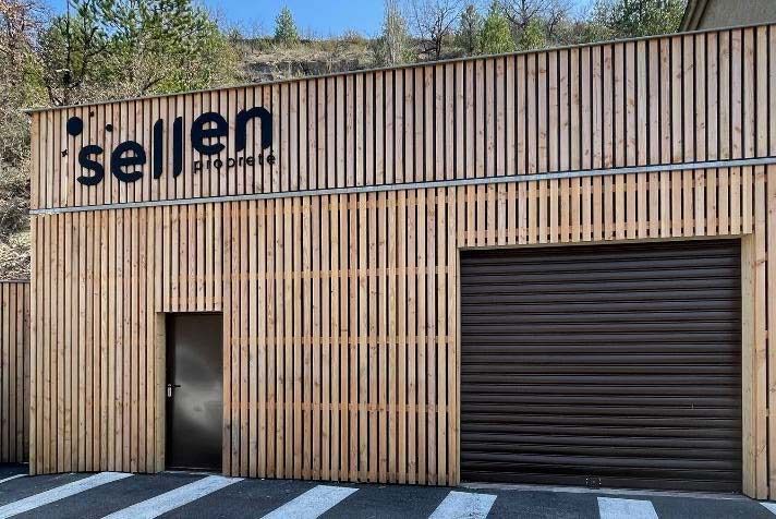 Bâtiment en bois avec une enseigne « sellen », une porte et une porte de garage fermée.