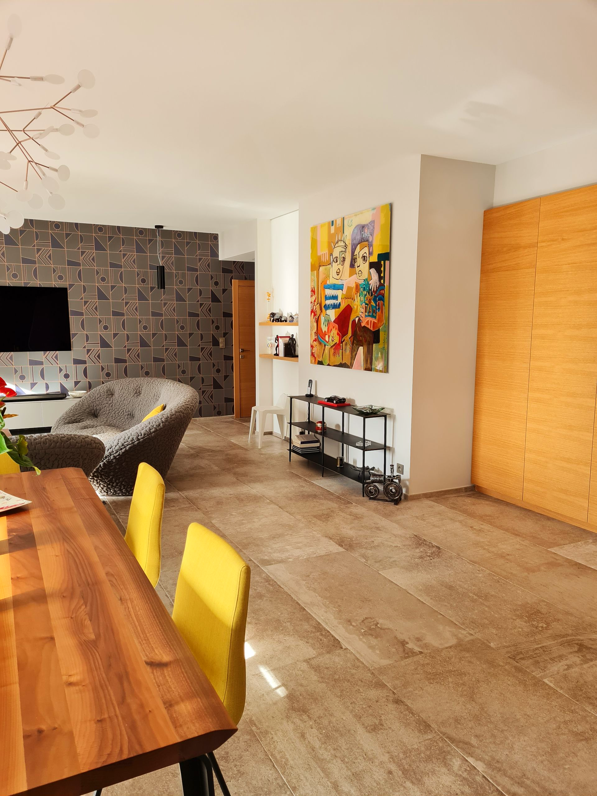 Salle à manger avec table en bois, chaises jaunes et fleurs rouges. Balcon en arrière-plan.