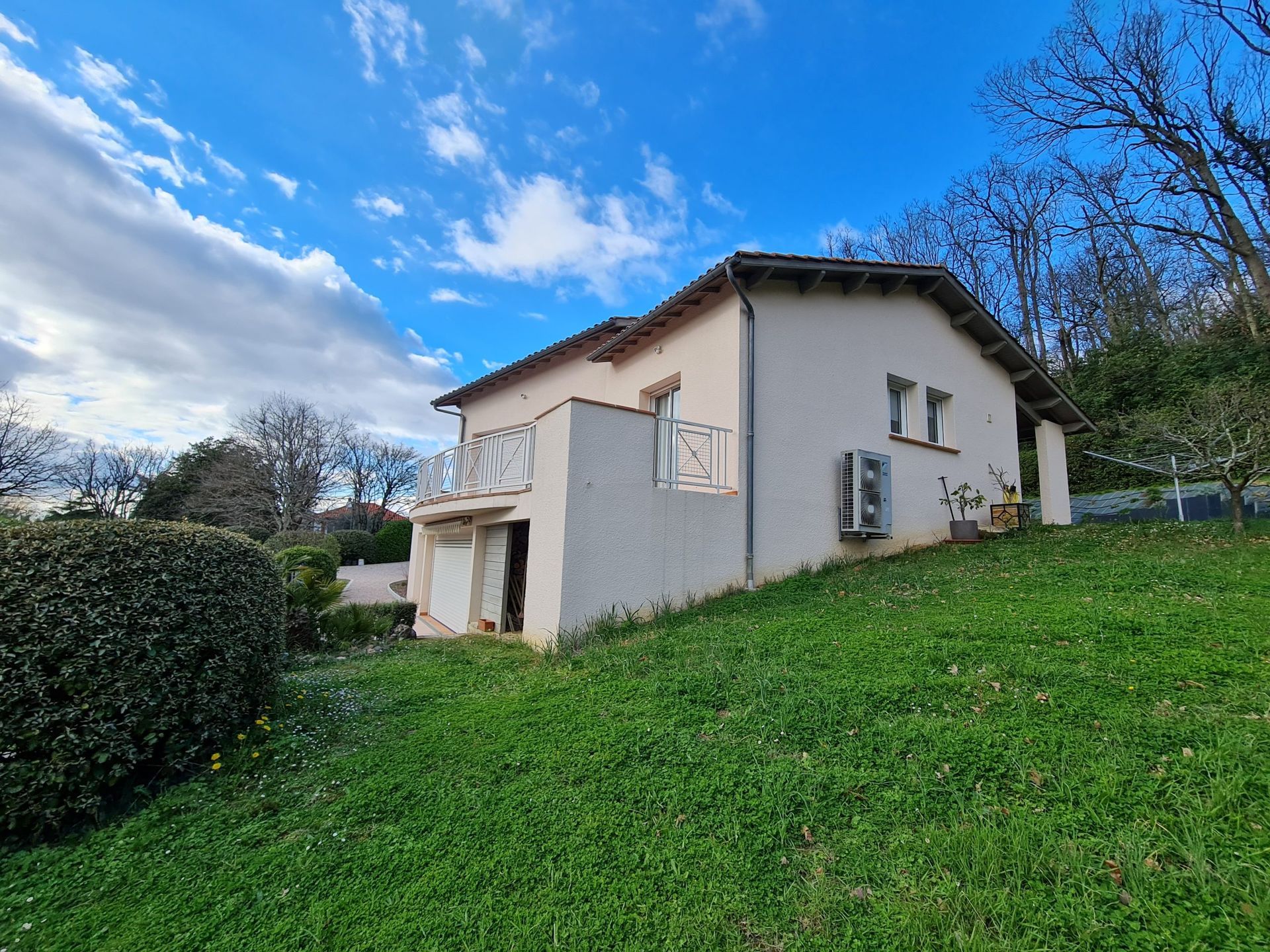Maison beige sur une colline herbeuse sous un ciel bleu nuageux.
