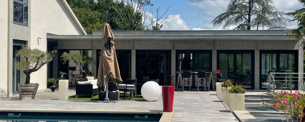 Terrasse avec piscine, sièges extérieurs et un bâtiment moderne sous un ciel bleu.