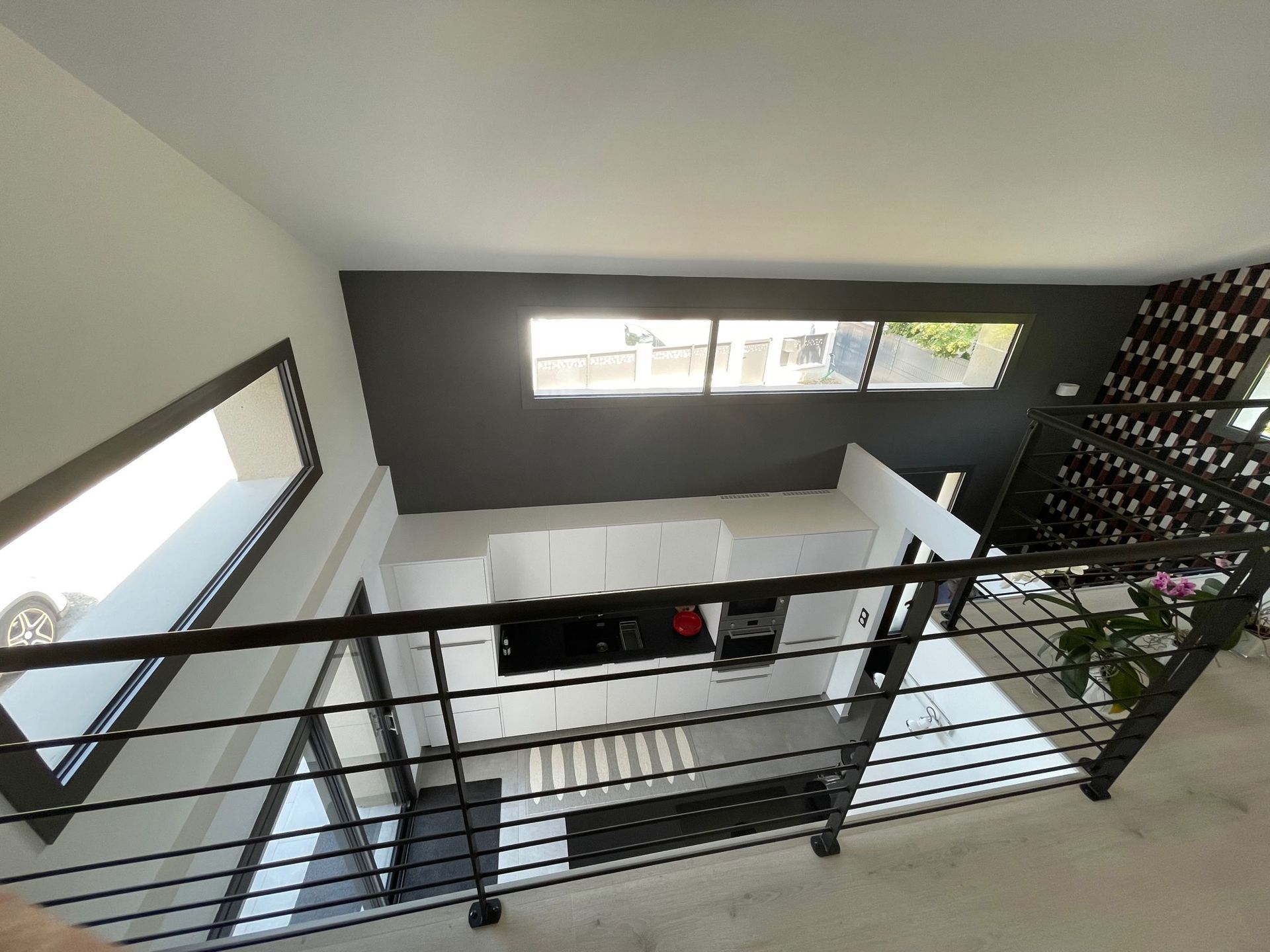 Vue intérieure d'un loft moderne avec une rambarde, un mur d'accent foncé et une cuisine en dessous.