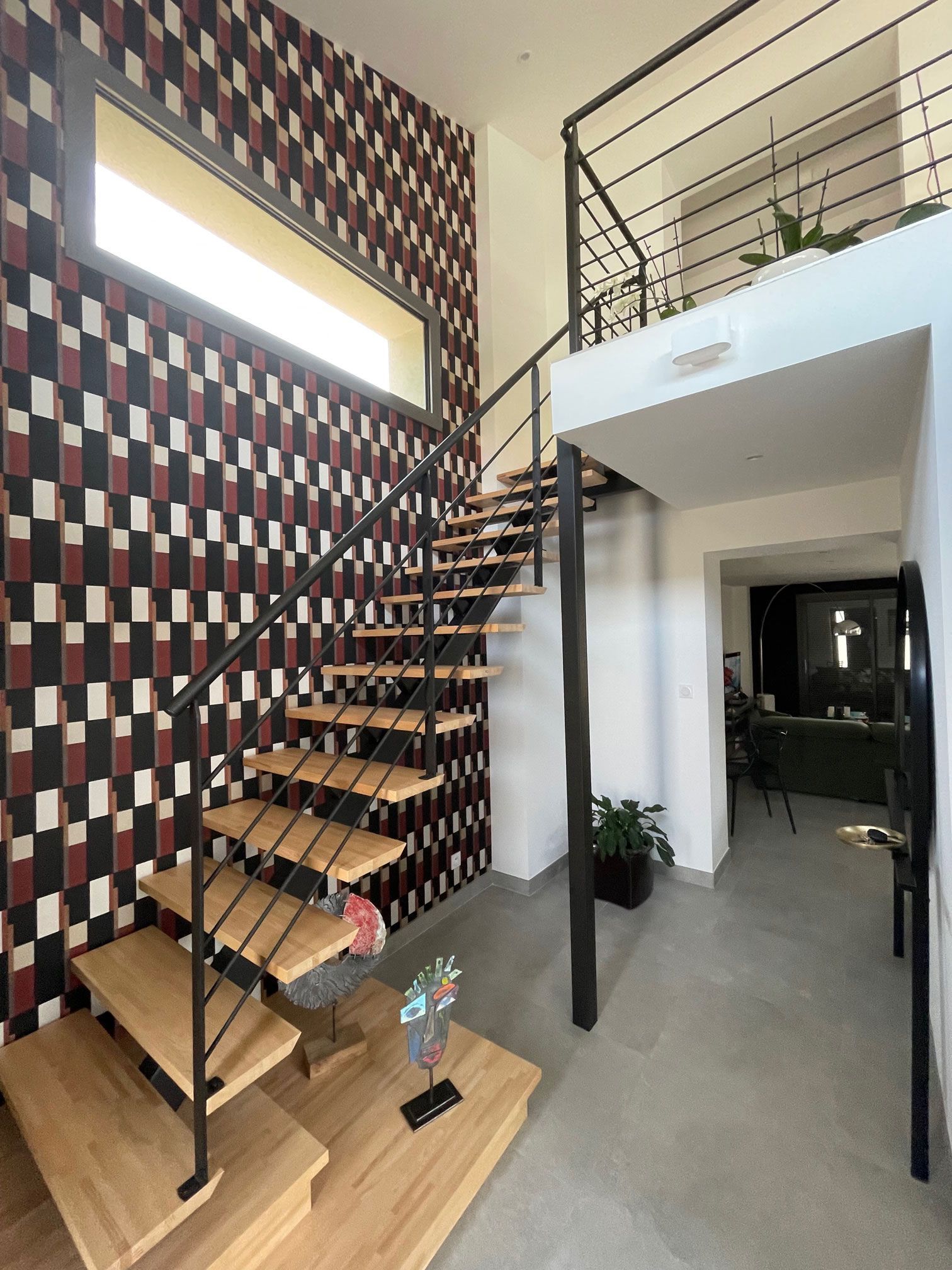 Intérieur avec escalier en bois, mur d'accent géométrique et rampe en métal. Espace lumineux et ouvert.