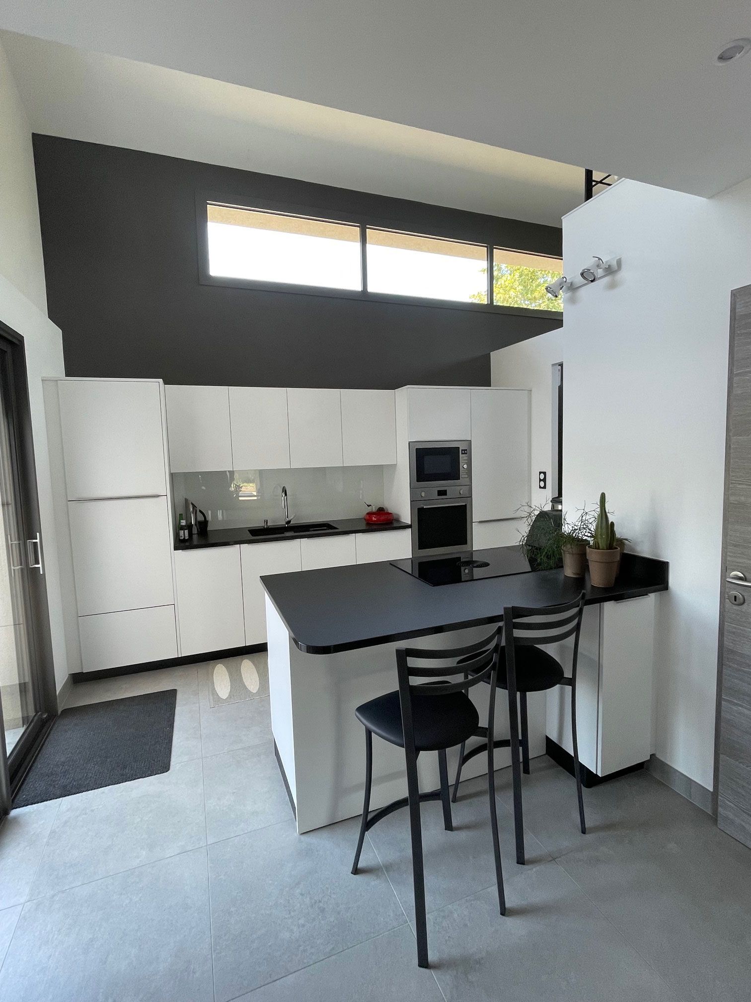 Cuisine moderne blanche avec îlot central, comptoirs noirs et deux tabourets de bar.