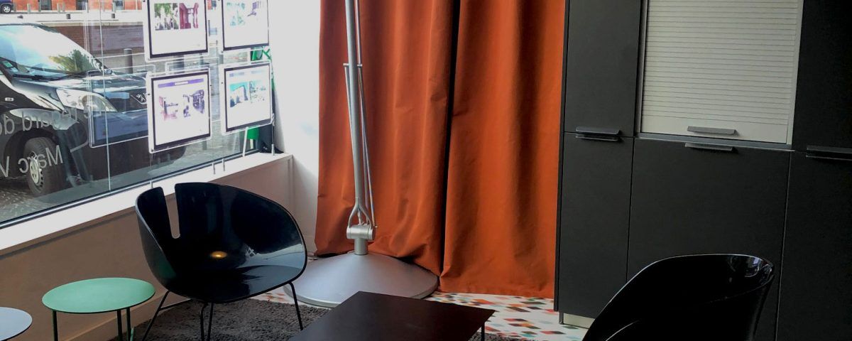 Intérieur avec chaises noires, rideau orange, lampadaire argenté et fenêtre donnant sur une voiture.