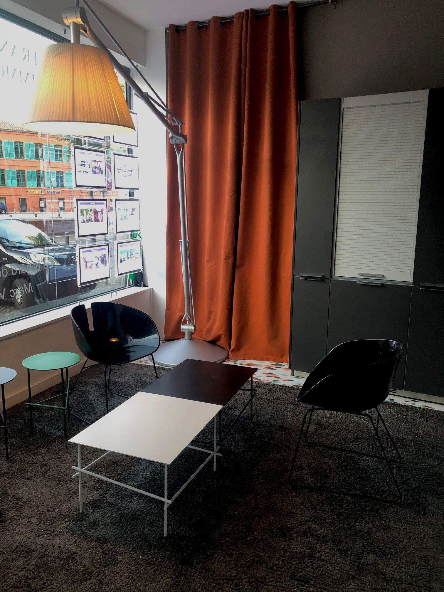 Salon moderne avec une table basse noire et blanche, des chaises incurvées, un lampadaire et une fenêtre offrant une vue sur la ville.