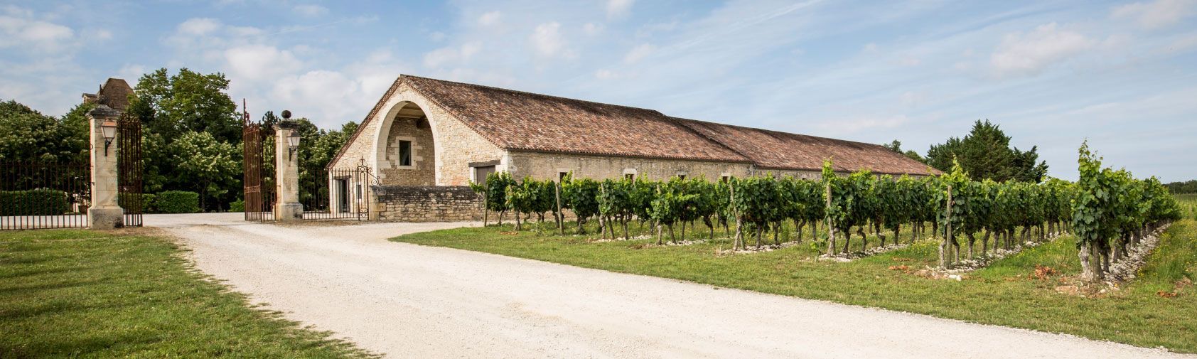 Vignoble avec un long bâtiment en pierre et des rangées de vignes au premier plan.