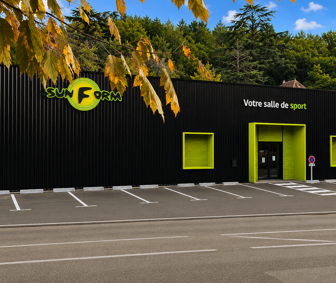 Bâtiment noir avec des touches de vert, logo « SUN FORM », voitures garées, arbres en arrière-plan.