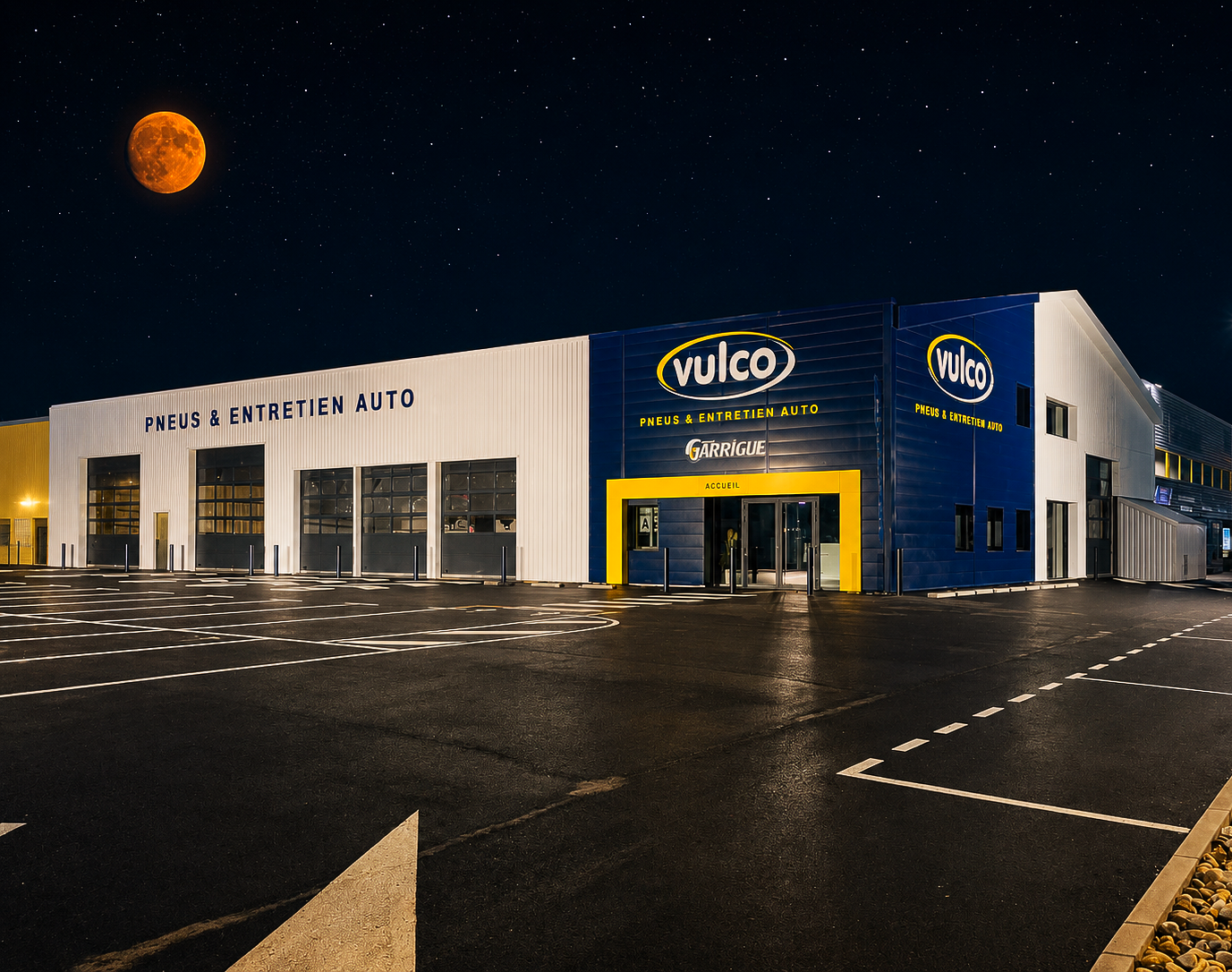 Extérieur d'un garage Vulco, de nuit. Le bâtiment est bleu et blanc avec des touches de jaune