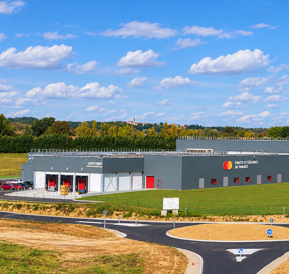 Un entrepôt logistique moderne de fruits et légumes est implanté dans un paysage rural verdoyant.