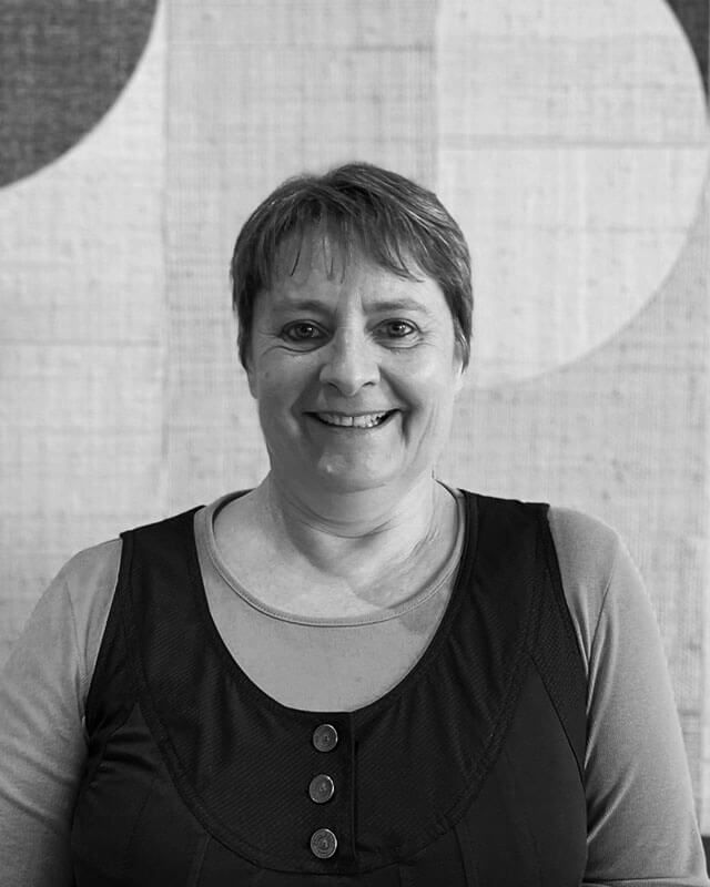 Femme souriante, vêtue d'un débardeur à col rond. En arrière-plan, un mur à motifs.