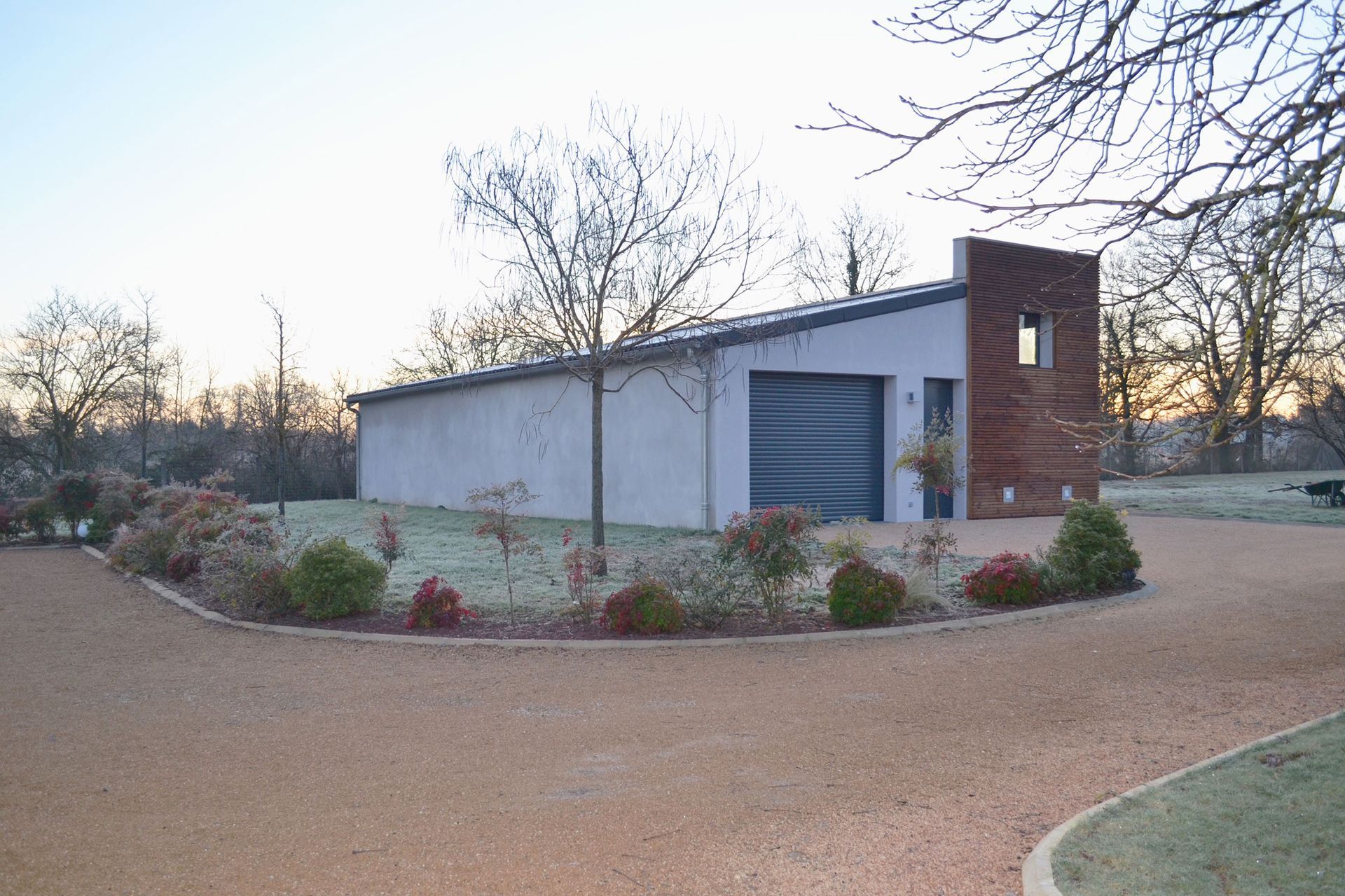 Petit bâtiment moderne avec une allée de gravier et de petites plantes, se détachant sur un ciel arboré.