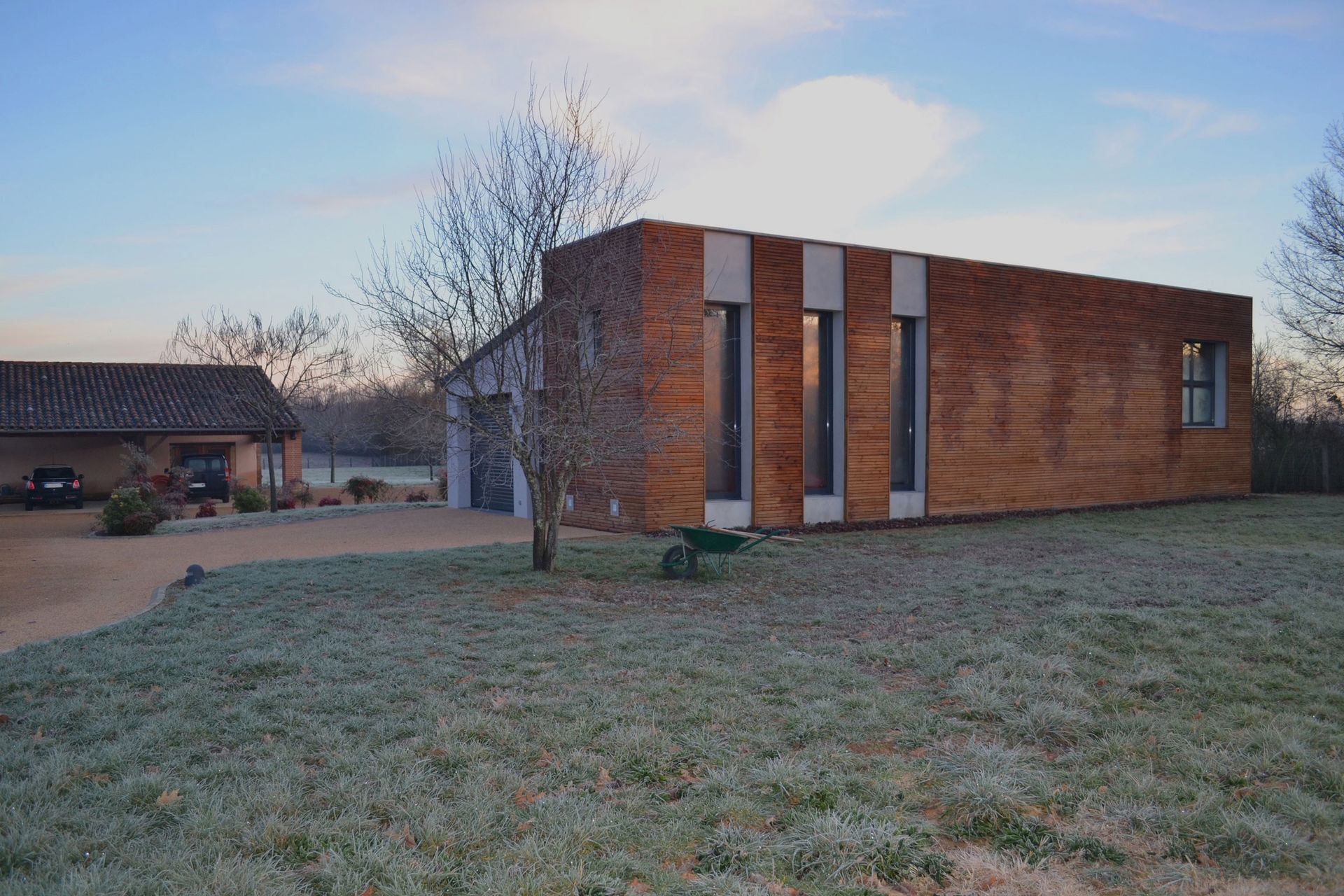 Bâtiment moderne rectangulaire en briques avec trois hautes fenêtres, herbe givrée devant.
