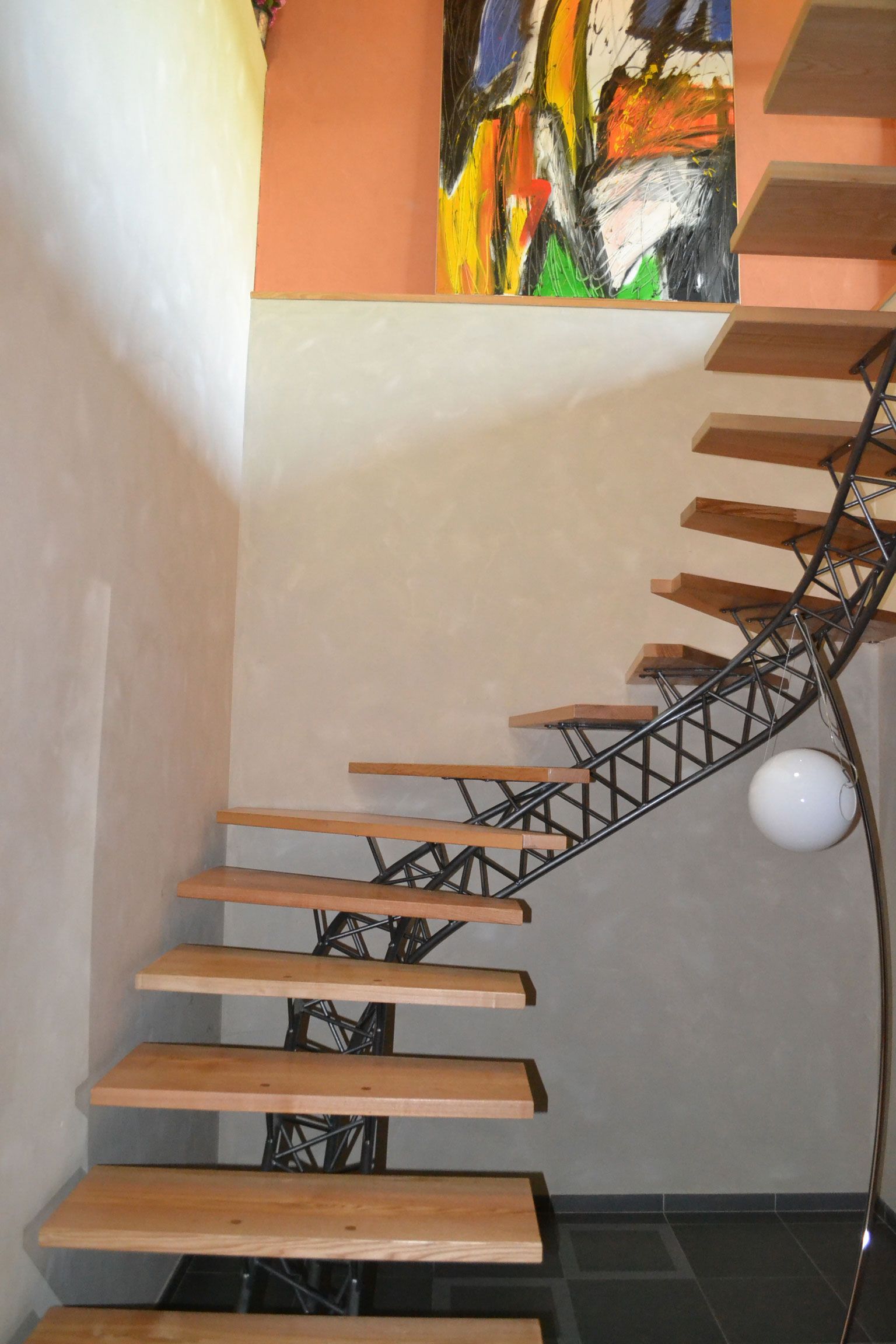 Escalier en bois avec rampe en métal noir ouvragée, menant à l'étage. Œuvre d'art abstraite et colorée.